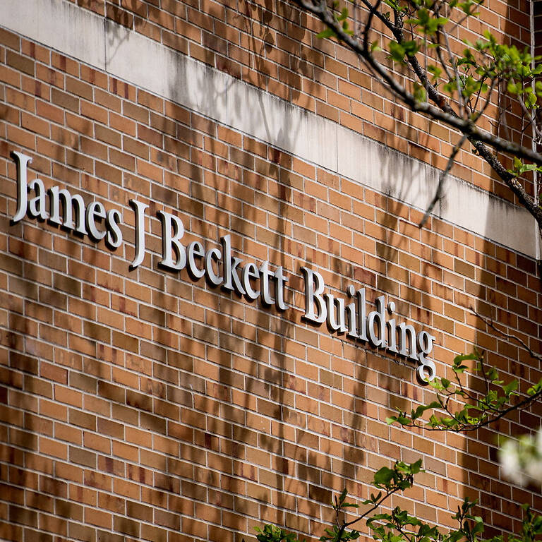 A brick building with "James J. Beckett Building" signage is partially framed by flowering trees in bloom.